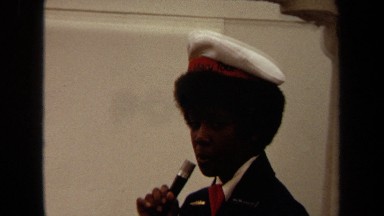 1971: a black woman wearing a uniform stands in front of a vintage car