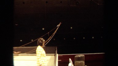 1971: woman wearing yellow and white suit looks up at huge ship hull and waving