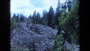 1971: a structure juts out of a rock face on a cliff in the woods MAINE