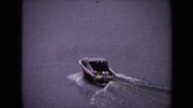 1970: a small, dark colored speedboat speeds across a river in a city WASHINGTON