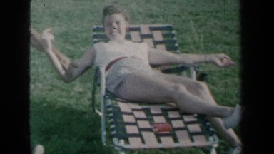 1959: Girl in White Shirt Lying on Grass as Men Sit and Talk