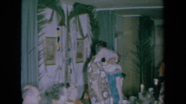 1961: Woman Places Garland Around Standing Man and Woman's Neck at Table