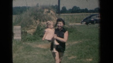1959: A Lady Dressed in Black Carries a Girl in Pink Across a Yard New York