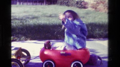 1979: Child Sitting in Small Red Wagon Pointing on California Sidewalk