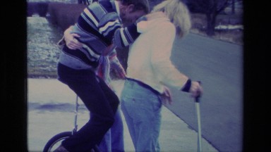 1977: people outside on road trying to tackle riding a one wheeled object