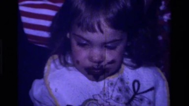 1979: a small seriously eating some cakes with her hand and tasting her fingers