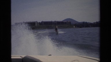 1977: a ski boat pulls a skier through a lake that has buildings lining