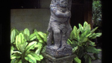 1984: Carved Warrior Statue in Ceremonial Outfit Carries Club with Fierce Eyes
