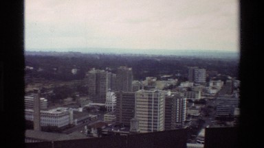 1983: aerial of city blocks downtown with multi-story buildings, industrial