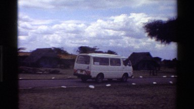 1983: a white van driving down a dirt road past some cabins