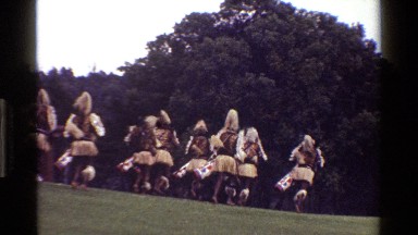 1983: tribesmen running down a hill with ornate drums past a building KENYA