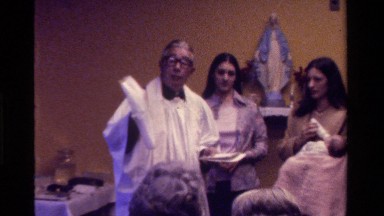 1975: the parish priest explains the symbolism of a baby's garments to onlookers