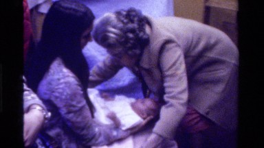 1975: an old lady is just covering a small kid as women holding the kid watches