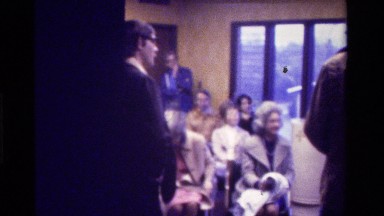 1975: a group of people gathered in a metropolis building with a priest