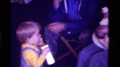 1975: two children, one standing and one carried by his mother