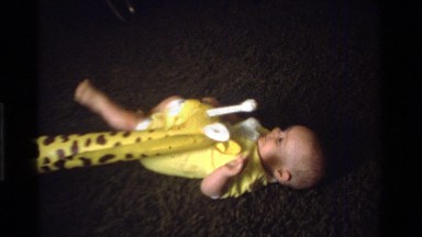 1975: baby laying on pillow on a living room floor with a big yellow inflatable