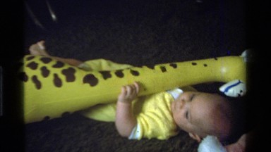 1975: Baby Laying on Pillow on Living Room Floor with Big Yellow Inflatable Giraffe