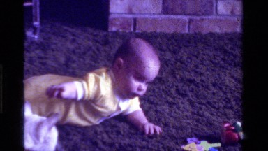 1975: a baby laying on it's stomach on the floor tries to play with a cat