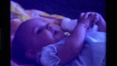 1975: a baby holding her bottle of milk laying down CALIFORNIA