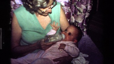 1977: older lady (maybe grandma) giving a bottle to a baby (probably girl)