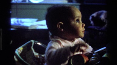 1977: a baby in a highchair is reaching out to the operator of the camera