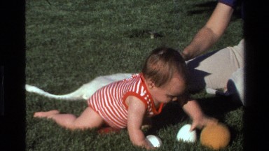 1977: baby crawling around on the grass playing with toys while being tickled