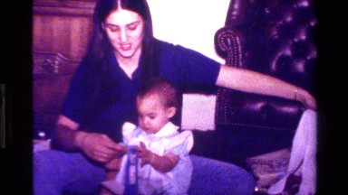 1977: baby in blue ruffled dress with ruffled pinafore, playing with wrapping
