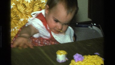 1977: baby reaches for piece of cake, takes a bite, smiles and drops frosting