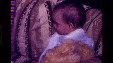 1977: zooming in on a baby sitting down a couch holding a teddy bear. CALIFORNIA