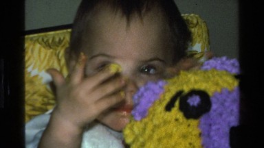 1977: a baby eats food that is yellow while you touching a multi colored yarn