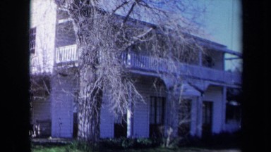 1969: Leafless Trees Stand Outside White Clapboard House with Second Floor Terrace