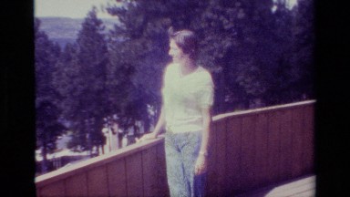 1977: Woman Leans on Terrace Fence Overlooking Low and Oblong Buildings