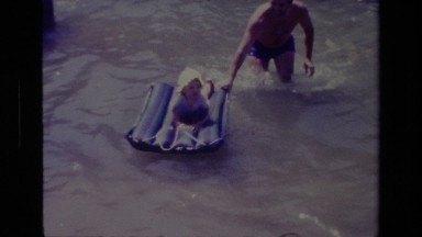 1978: father pushing infant child on inflatable raft on the river CANYON LAKE