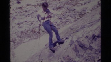 1975: woman attached to rope climbing down a hill and backpackers hiking