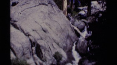 1975: a waterfall flows down among huge rocks in the forest. MINARET WILDERNESS