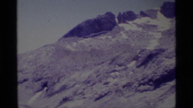 1975: mountain peaks with a little snow; people backpacking in rocky area