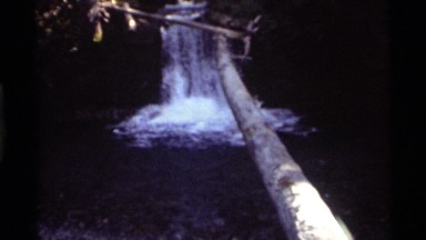 1972: waterfall beneath a bridge of tree trunks into a pool of water. HOLLAND