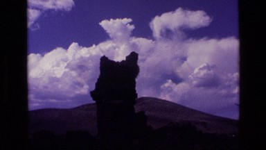 1972: natural formation tilts and reaches up toward blue sky and puffy cloud