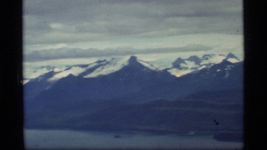 1977: snowy mountains and a cloudy sky as seen from the window of a plane.