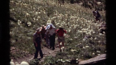 1977: a group of people walk in a single file line up a hill SAPPHIRE LAKE