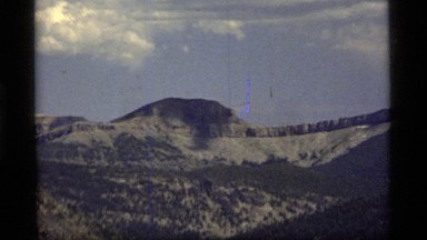 1977: a mountain peak rises above surrounding mountains and juts into a blue sky