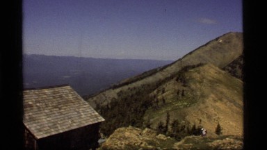 1977: man walking to a house amongst the mountains SAPPHIRE LAKE MONTANA