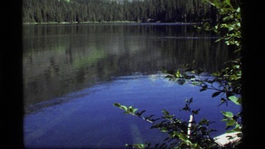 1977: serene lake surrounded by an evergreen forest and mountains SAPPHIRE LAKE