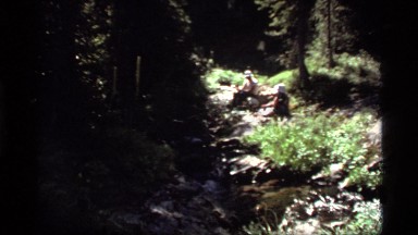 1977: two people sit on rocks next to a small stream in a hilly, forested area