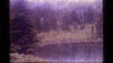 1977: Group of People Walking by a Body of Water Through Trees, Fog and Brush