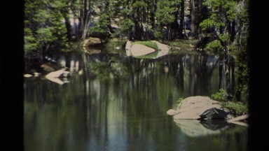 1978: tranquil pond reflects partly submerged gray rocks and surrounding green