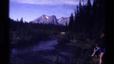 1979: two people are enjoying sitting near water flow with a faraway mountain