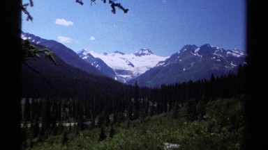 1979: beautiful valley with a forest and snow covered rocky peaks beyond