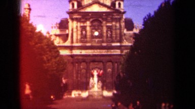 1939: statue of white figures stands in front of domed building with clock