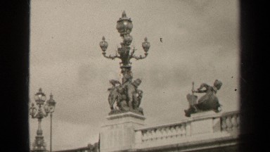 1947: detailed lamp posts on a bridge followed by a man dressed in black staring